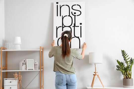 Young Woman Hanging Picture On Wall In Living Room