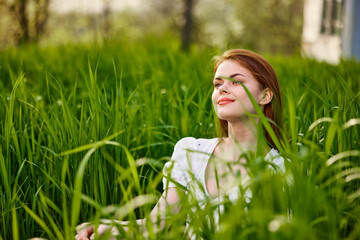 Naklejka na ściany i meble a young woman in a light summer dress enjoys nature sitting in the tall grass