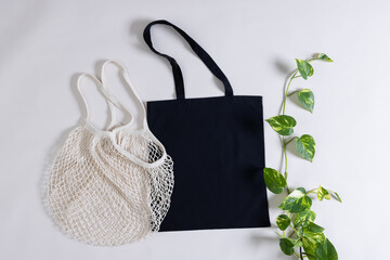 High angle view of white net and black canvas bag with copy space and plant on white background