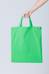 Hand of caucasian woman holding green canvas bag with copy space on grey background