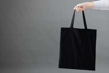 Hand of caucasian woman holding black canvas bag with copy space on grey background