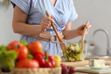 Obraz na płótnie Canvas Young woman making vegetable salad in kitchen, closeup