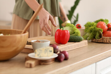 Obraz na płótnie Canvas Mature woman making vegetable salad at table in kitchen, closeup