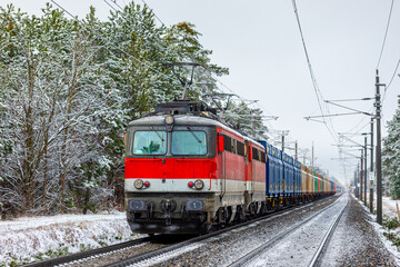 Red locomotive pulls a freight train. Snow. Forest. European railways