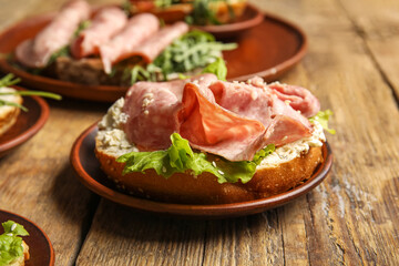Tasty ham bruschetta with lettuce on wooden background