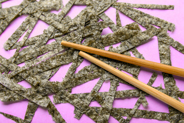 Cut nori sheets and chopsticks on lilac background, closeup