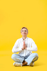 Mature woman meditating on yellow background