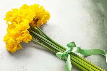 Beautiful narcissus flowers with green ribbon on color grunge background