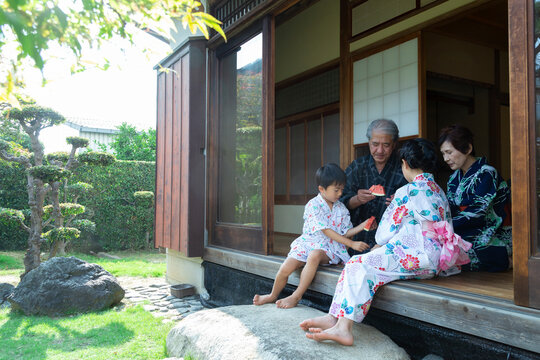 縁側でスイカを食べる祖父母と孫