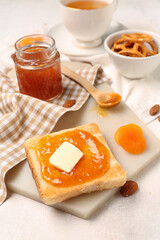 Board of tasty toast with apricot jam on light background