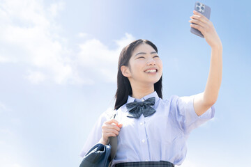 青空の中自撮りをしたりスマホで撮影をする女子高生