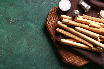 Wooden board with tasty Italian Grissini on green background