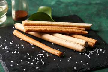 Slate board with tasty Italian Grissini on green background, closeup