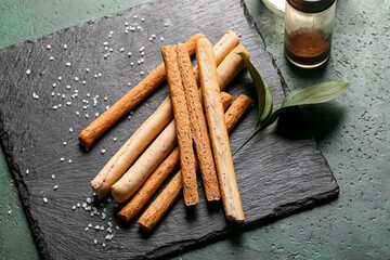 Slate board with tasty Italian Grissini on green background