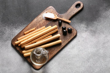Wooden board with tasty Italian Grissini on grunge background