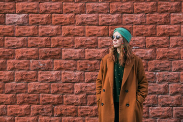 Portrait of a young 30+ hipster woman in sunglasses and stylish clothes in the city against a brick wall. Modern lifestyle.