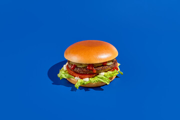 A minimalist-style burger with beef patty, lettuce, tomato, ketchup, pickles, and white sauce on a...