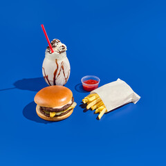 Combo meal with burger, fries, sauce, and milkshake on a blue background. Minimalist fast food...