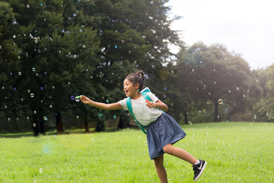シャボン玉を捕まえようとしているランドセルを背負った小学生の女の子