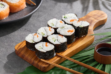 Simple roll yin yang maki on wood on gray stone background. Maki sushi with salmon and cucumber with chopsticks. Aesthetic composition with Yin yang maki sushi on concrete table. Asian food concept