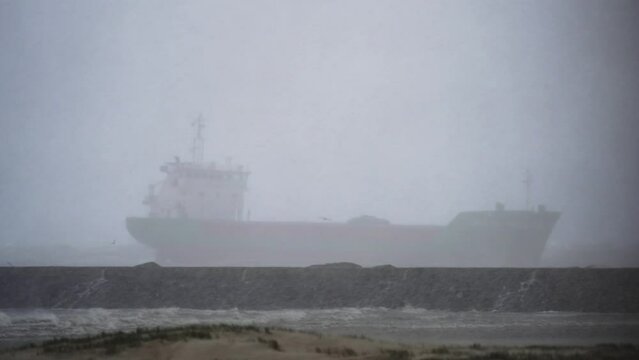 Large empty cargo ship braving stormy weather on sea in misty conditions