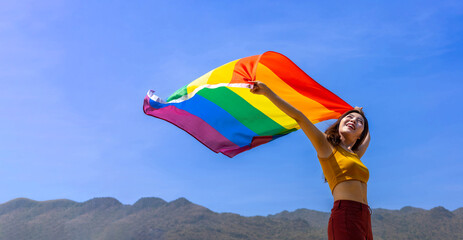 Woman holding colorful rainbow flag is dancing in homosexual parade for LGBTQ+ pride month and coming out of the closet concept for gender fluid and sexual equality freedom concept