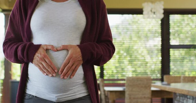 Midsection of caucasian pregnant woman gesturing heart over belly