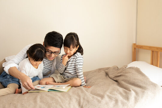 ベッドの上で父親に絵本を読んでもらう姉妹