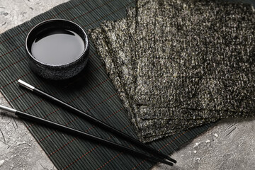 Bamboo mat with nori sheets, soy sauce and chopsticks on grunge background, closeup © Pixel-Shot