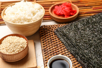 Wicker mat with nori sheet, rice, sesame seeds, ginger and soy sauce on table, closeup
