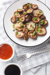 Fried shiitake mushrooms close-up on a plate served with chili and soy sauces on a wooden table. Vertical top view from above