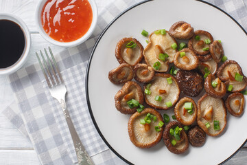 Appetizer fried shiitake mushrooms with green onions close-up on a white plate on the table. Horizontal top view from above