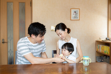 母親の膝の上に座り父親にバナナを食べさせてもらう子ども