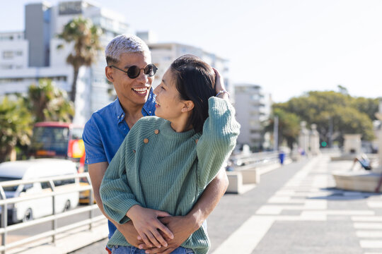 Happy diverse couple spending time together, embracing on promenade by the sea