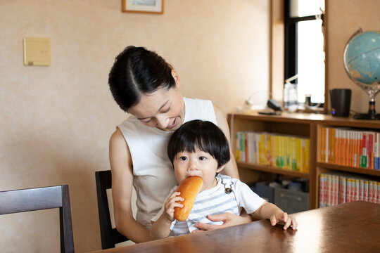 母親の膝の上でパンを食べる子ども