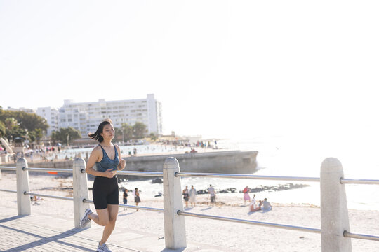 Happy asian woman wearing sportswear and running on promenade by the sea