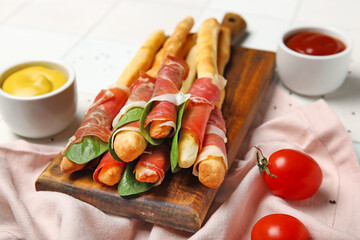 Fototapeta na wymiar Wooden board of tasty Italian Grissini with bacon on table, closeup