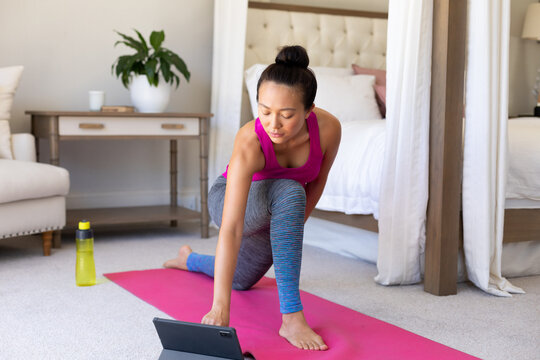 Happy asian woman doing yoga, stretching and using tablet in bedroom