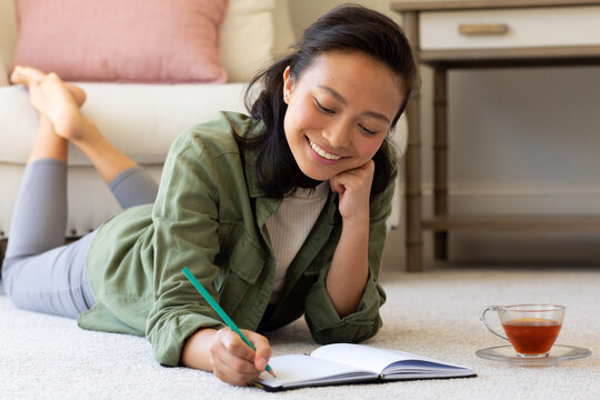 Happy asian woman writting in notebook on floor in bedroom