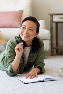 Happy asian woman writting in notebook on floor in bedroom
