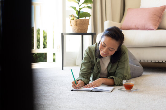 Happy asian woman writting in notebook on floor in bedroom