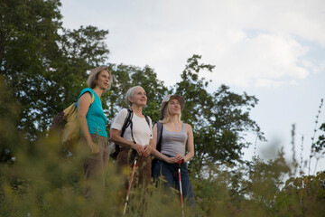 Naklejka na ściany i meble multi generation a group of women friends with backpacks standing on a mountain and spending time together. travel tourism concept. Outdoor activities on weekends.
