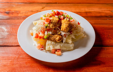 Traditional chicharrón dish with cassava and tomato salad. Latin food chicharron con yuca served on wooden table. Nicaraguan dish chicharrón with cassava on the table.