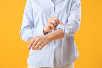 Young woman rolling up her sleeve on  yellow background