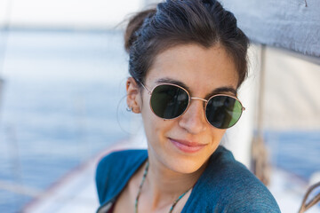 Happy smiling portrait of a beautiful young girl in sunglasses on a yacht or boat on the coast with the sea in the background.