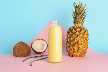 Glass bottle of tasty pineapple smoothie, straw and coconut on colorful background