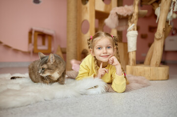 Cheerful girl lying on floor with fluffy cat over animal shelter background