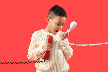 Little African-American boy with two telephone receivers on red background