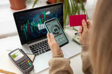 Beautiful carefree woman in casual showing credit card to camera while working with laptop
