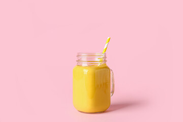Mason jar of tasty yellow smoothie with straw on pink background